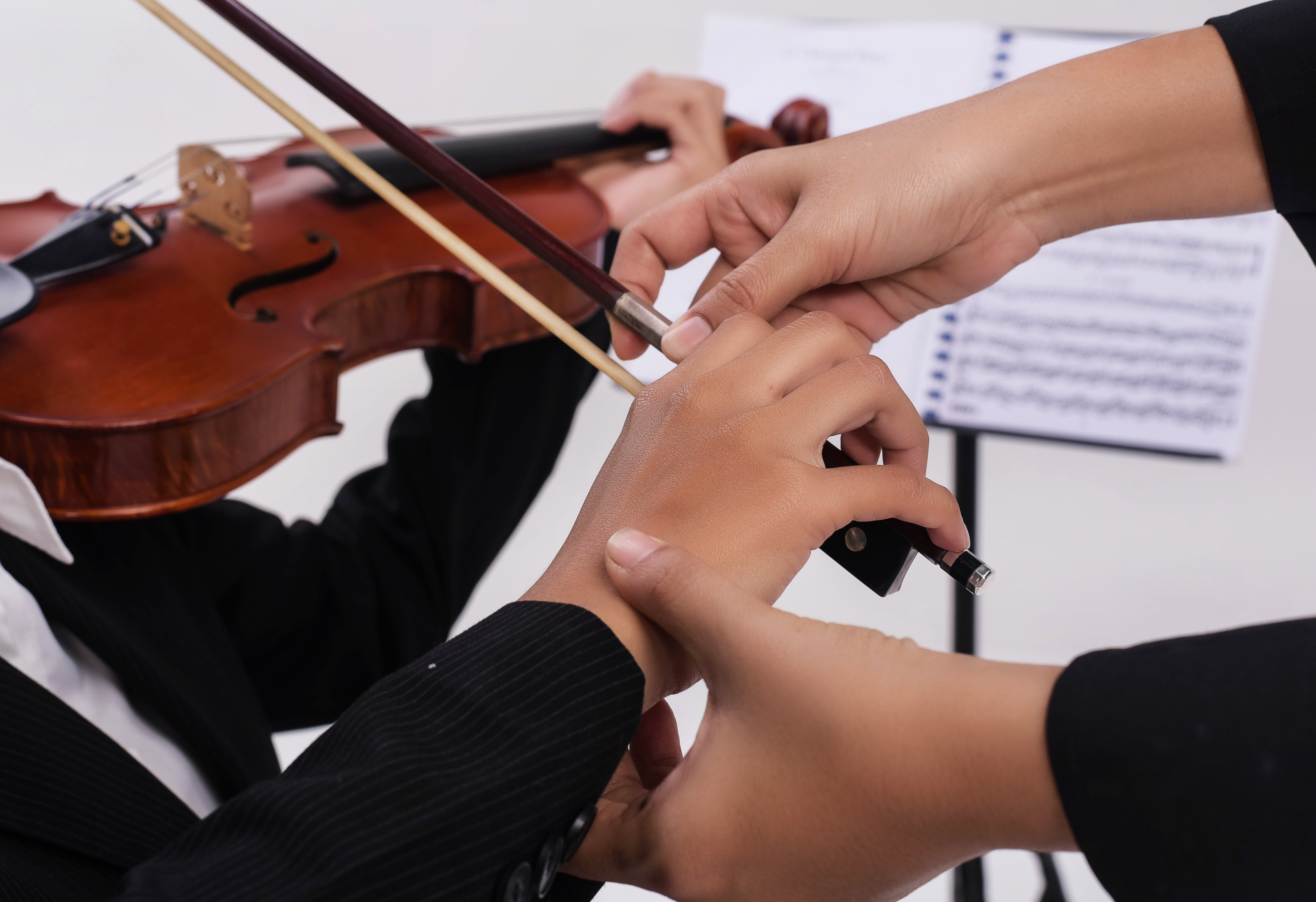 The violin teacher hands is teaching the violin student,by touch student hand for using bow to play on string ,blurry light design background.